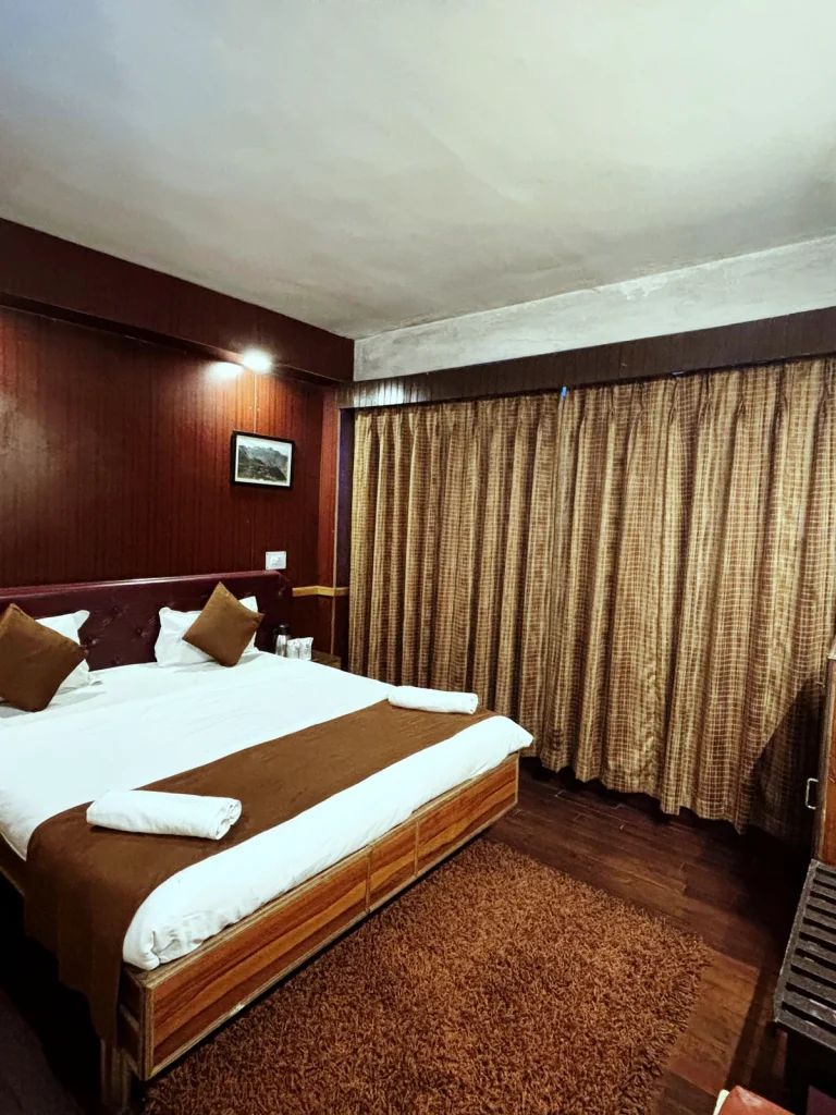 Guest room with dark wood panelling, a maroon tufted headboard and framed mountain prints at Hotel Apsara, Darjeeling